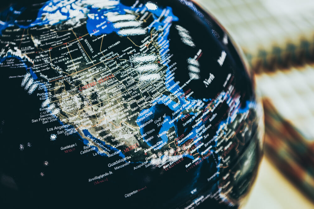 A close-up of a globe focused on North America, showing detailed country and city names across the United States, Canada, and Mexico, with surrounding oceans and parts of Central America visible.